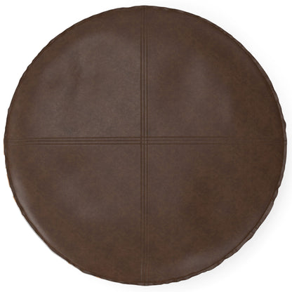 The Brody - Round Pouf is a dark brown leather cushion featuring visible stitched lines that form a cross pattern across its top surface.
