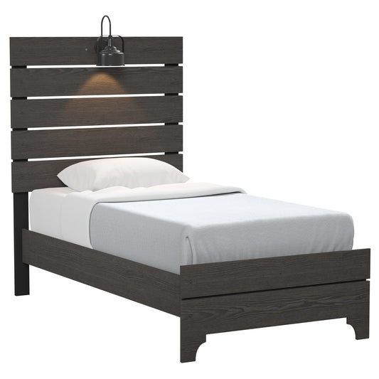The Junipe - Bed With Lights is a single bed with a dark wooden frame, slatted headboard, white pillow and sheets, light gray blanket, and a black wall-mounted lamp above the headboard for warm illumination.