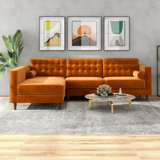 A modern living room featuring the Christian Mid-Century Modern Design Sectional Sofa in orange velvet, a round coffee table, gray rug, potted plant, and three abstract art pieces on a light gray wall.