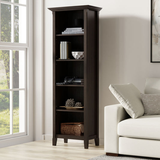 The Amherst 5 Shelf Bookcase in brown stands beside a white sofa in a bright living room with a large window, displaying books, decor, and a basket on its five spacious shelves.