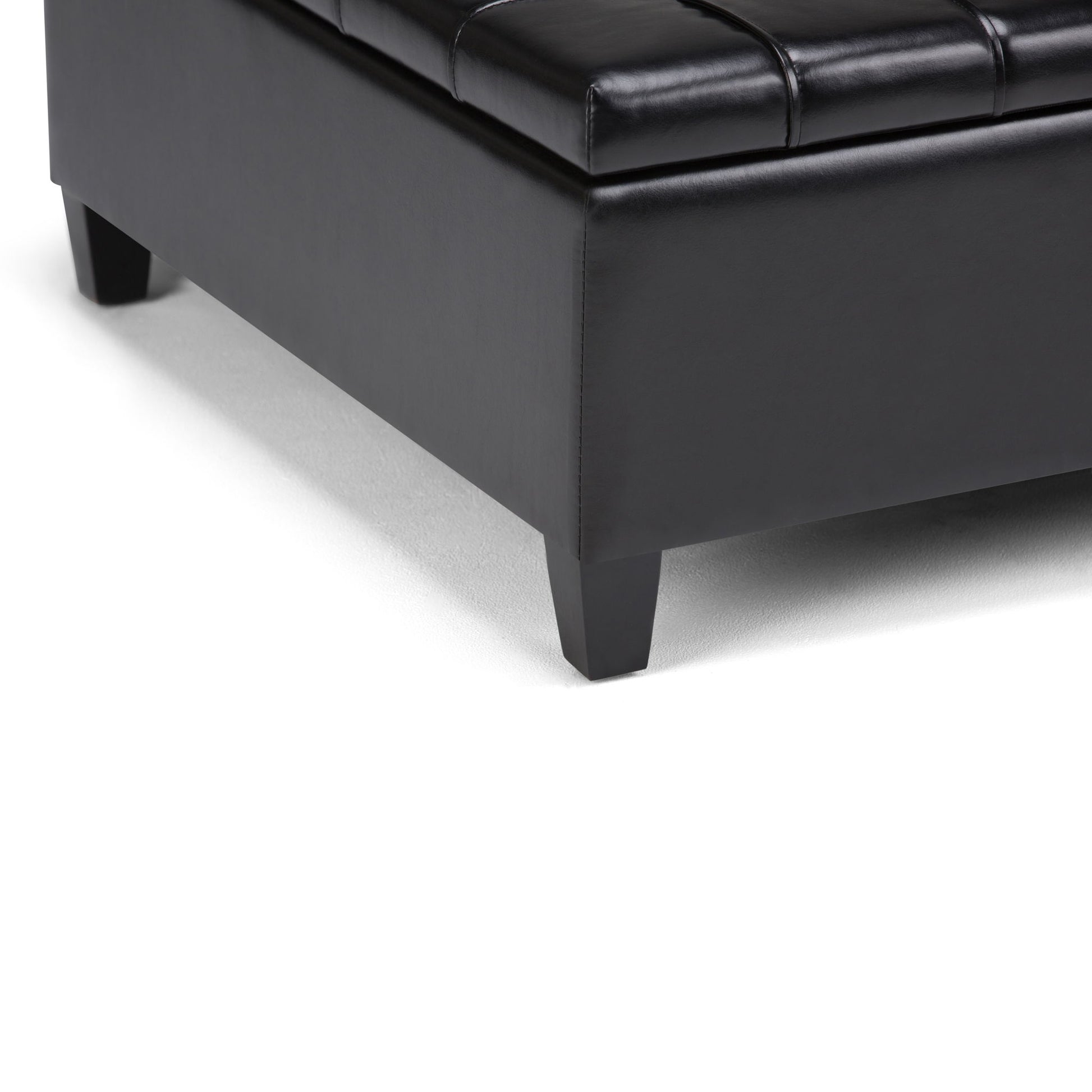 Close-up of the bottom corner of the Harrison - Large Coffee Table Storage Ottoman in black leather with short square wooden legs, placed on a white surface.
