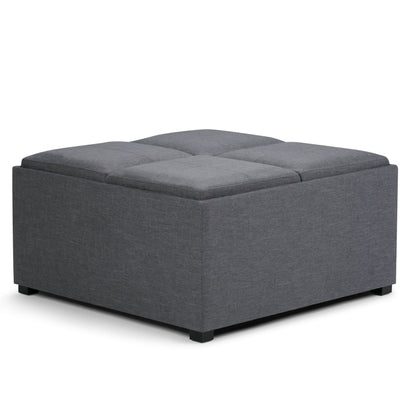 The Avalon Square Coffee Table, Storage Ottoman features dark grey upholstered fabric, a tufted top, and short black legs. It serves as a footrest, coffee table, or extra seating.