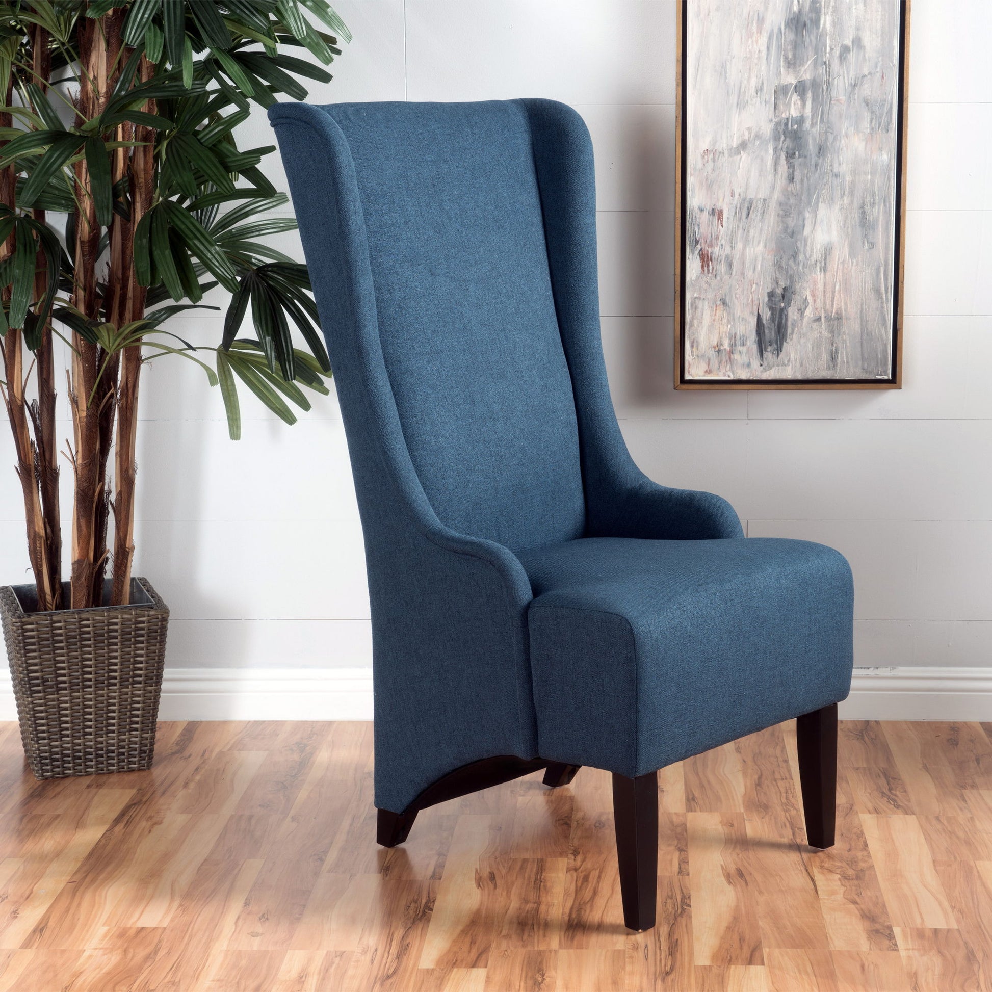A set of Alight upholstered dining chairs with high backs and birch wood legs sits on a light wood floor beside a potted plant, with an abstract painting hanging on the white wall in the background.