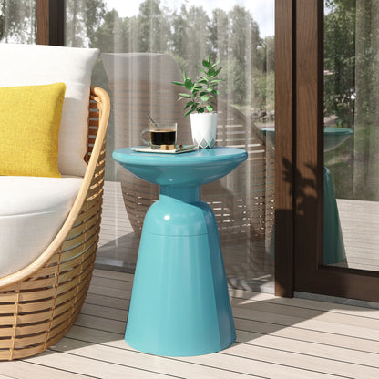 An Outdoor Modern Metal End Large Table holds a small potted plant and coffee cup beside a cushioned chair with a yellow pillow on a patio near glass doors with sheer curtains. Trees can be seen outside.