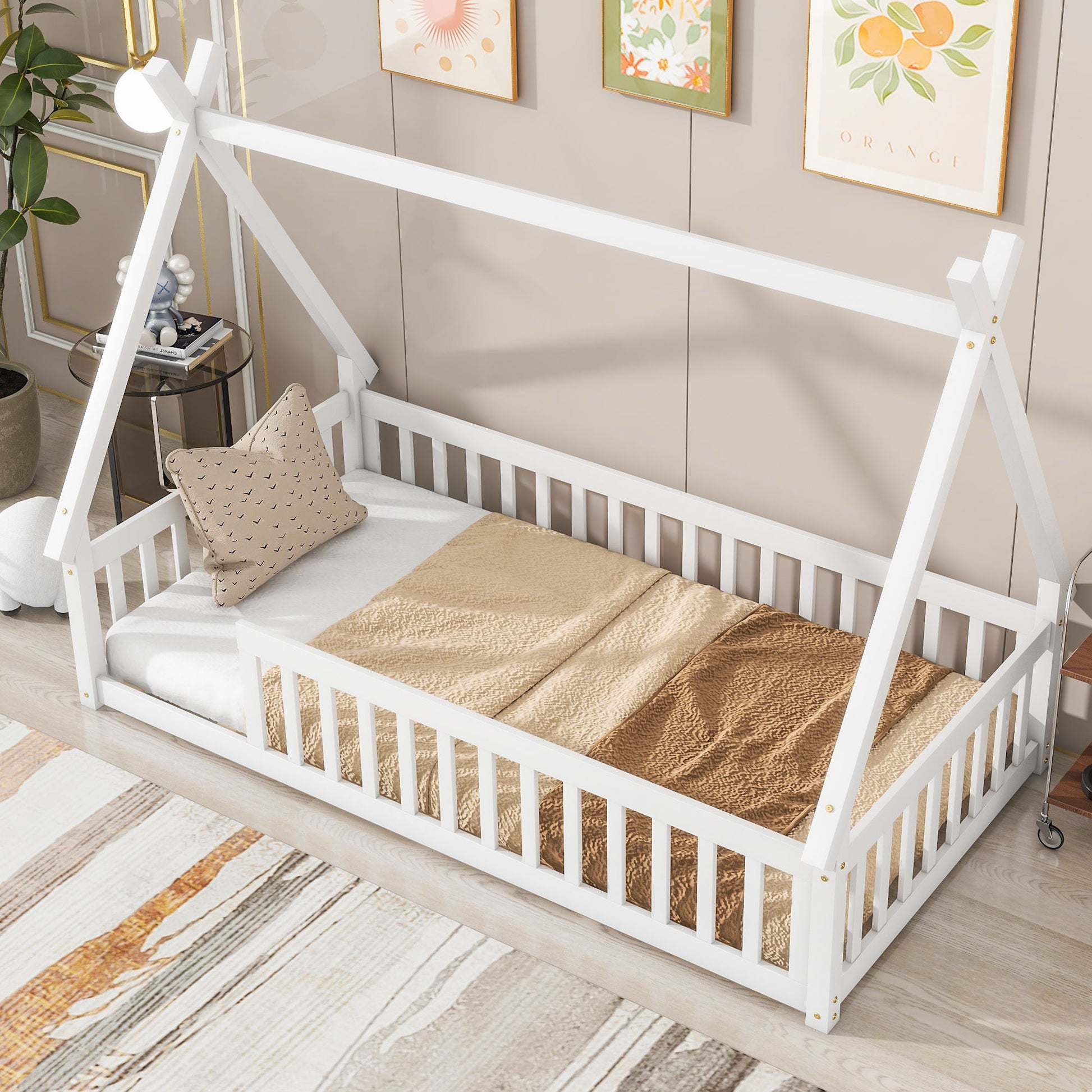 A Tent-Shaped Floor Bed with guardrails and slats, styled with beige and white bedding and a patterned pillow, sits in a cozy room accented by wall art, a rug, and decorative pieces.