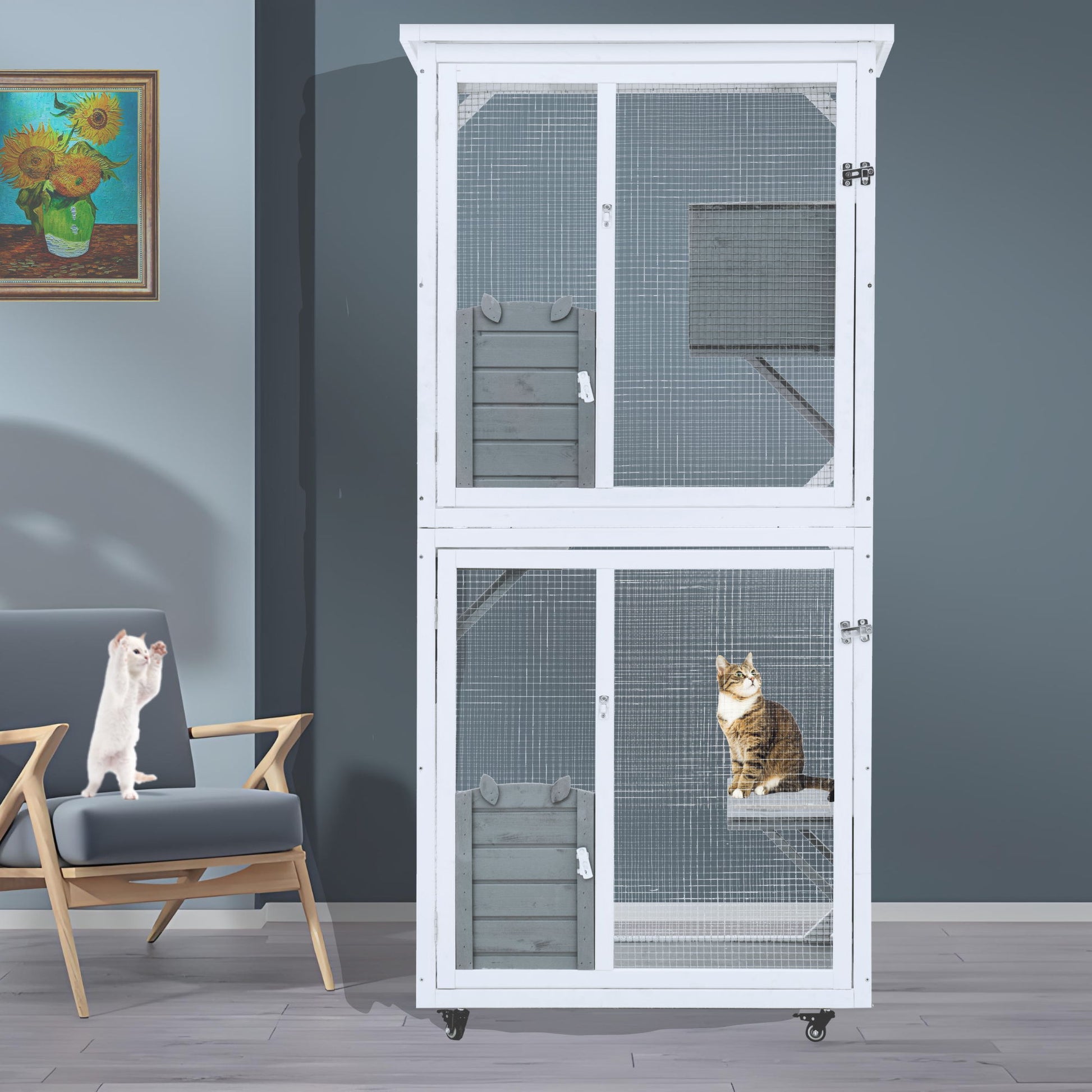 The Xpt016 Outdoor Indoor Cat Pet Climbing Rack Play Cage - White, with two sections, stands against a blue wall. A brown tabby cat is inside the lower section, while a white cat sits on a gray chair nearby beneath a sunflower painting.