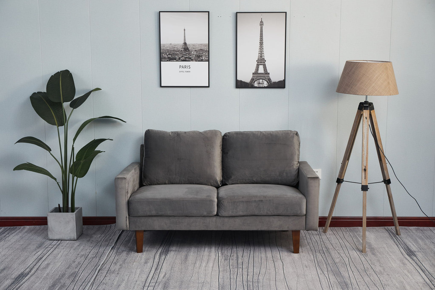 A modern living room with the Comfortable Loveseat With Durable Construction in gray, a tall potted plant on the left, two framed Eiffel Tower pictures on the wall, and a tripod floor lamp with a beige shade on the right.