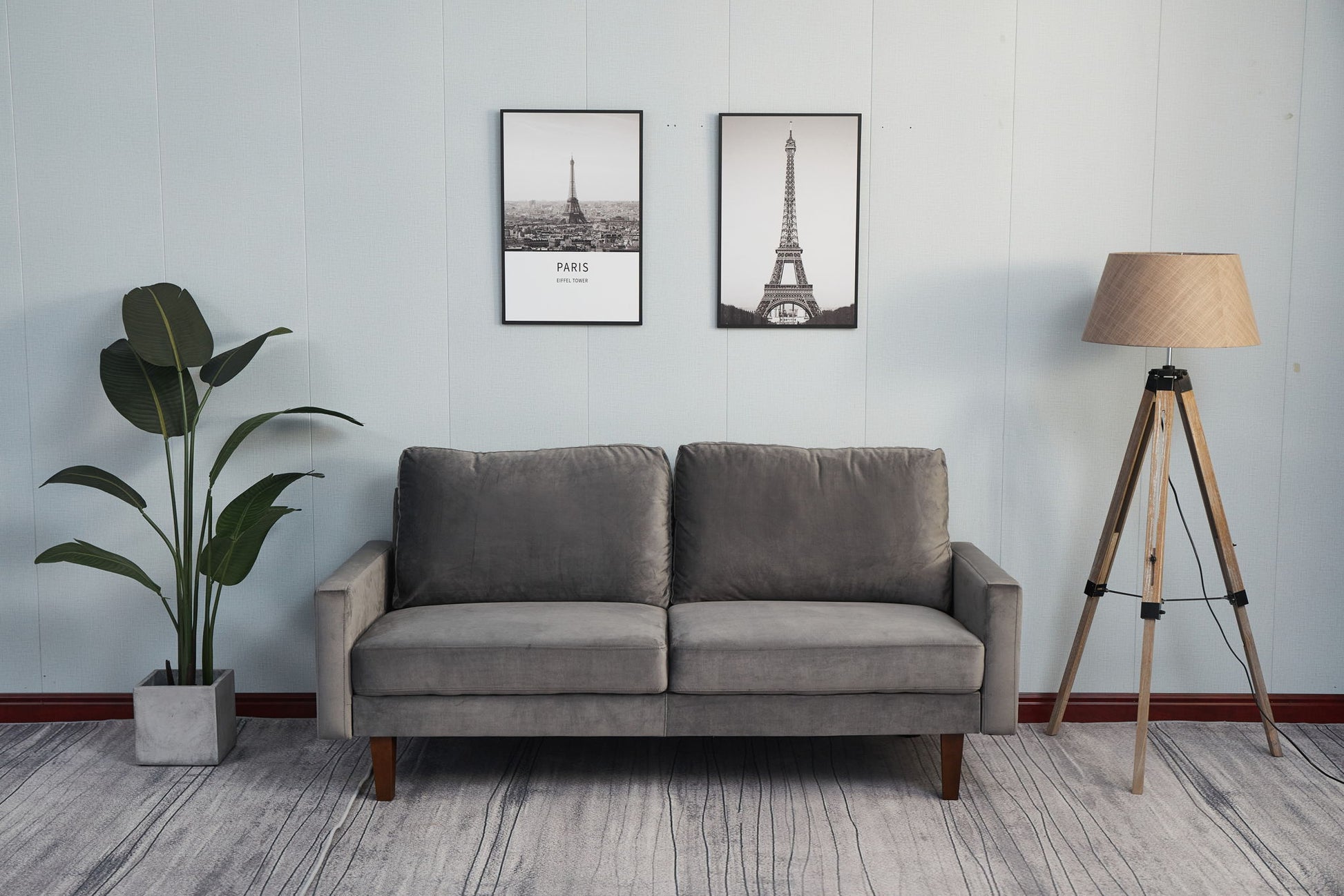 A minimalist living room features the Comfortable Loveseat With Durable Construction in gray, two framed Eiffel Tower prints on the wall, a potted plant to the left, and a wooden floor lamp with a beige shade on the right.
