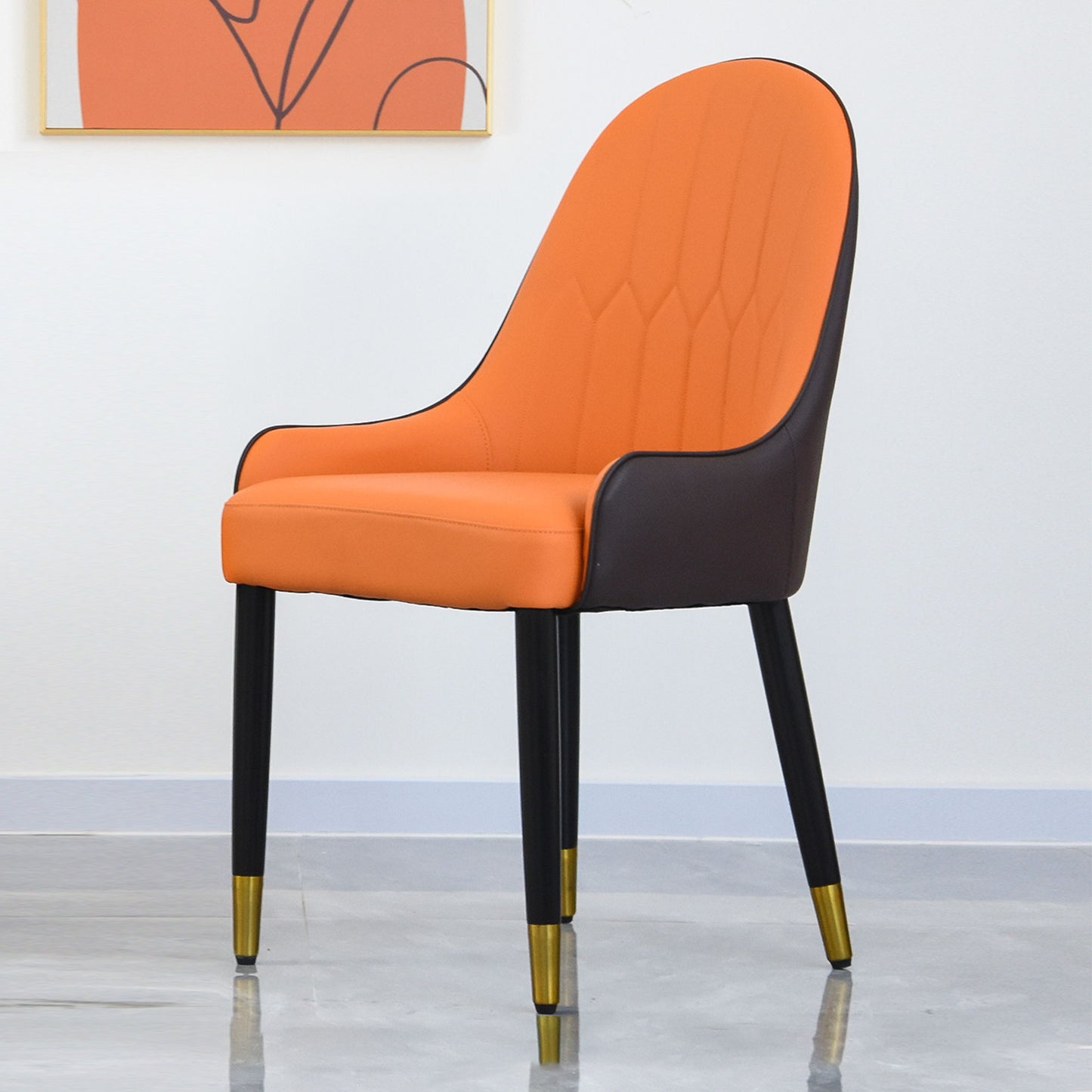 The Modern PU Sponge-Filled Dining Chair (Set of 2) features an orange cushioned seat and backrest, solid wood metal legs with gold tips, dark sides, and is ideal for restaurants, living rooms, or rooms. Shown on a gray marble floor with white walls and abstract art.