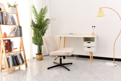 A modern, minimal home office with a beige Cross Legged Office Chair (swivel, height-adjustable), white desk with drawers, a bookshelf full of books, potted plant, floor lamp, and light gray tiled floor. Natural light streams in from the left.