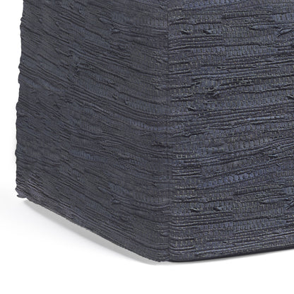 A close-up shows the dark charcoal gray textured surface of the Fredrik - Handcrafted Square Pouf, wrapping around its corner with horizontal, irregular lines and a rough, layered appearance.