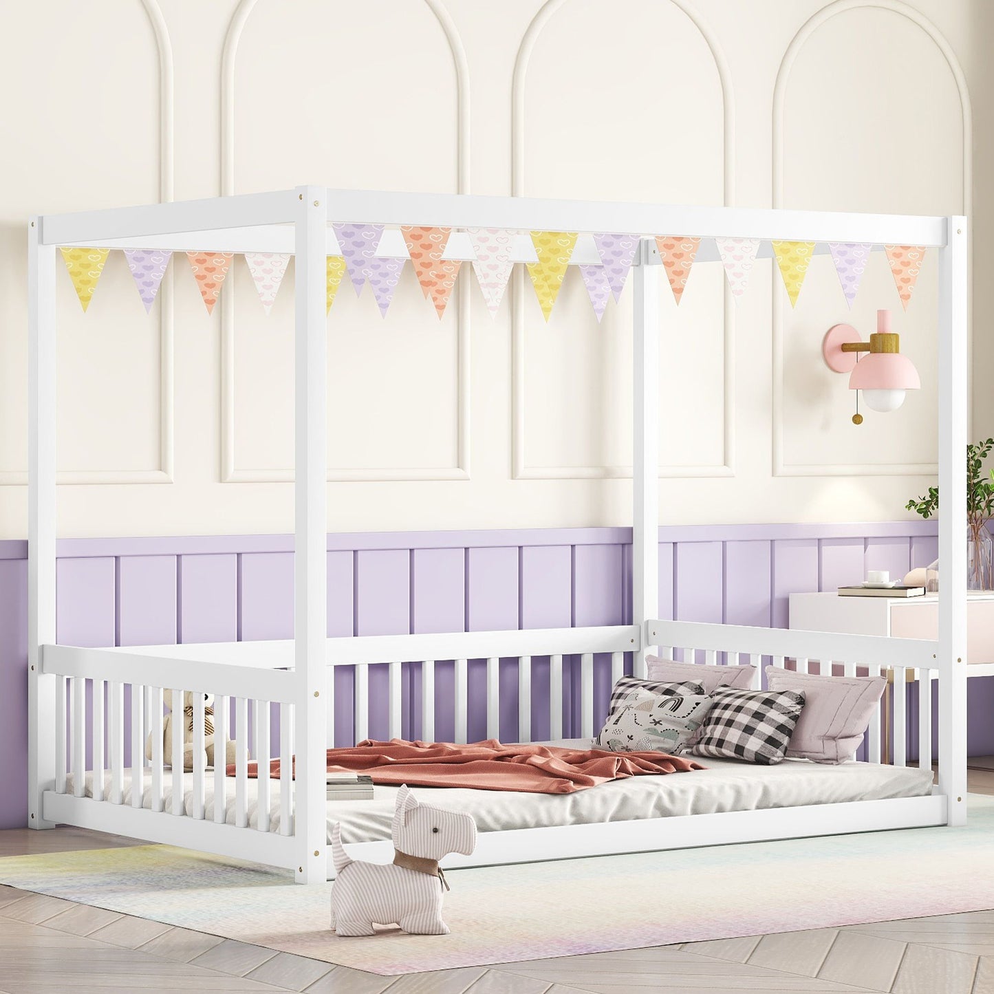 A Canopy Frame Floor Bed With Fence, guardrails, pastel pennant bunting, pink and gray bedding, a plush animal toy, in a lavender and white room with wainscoting and a pink wall sconce.