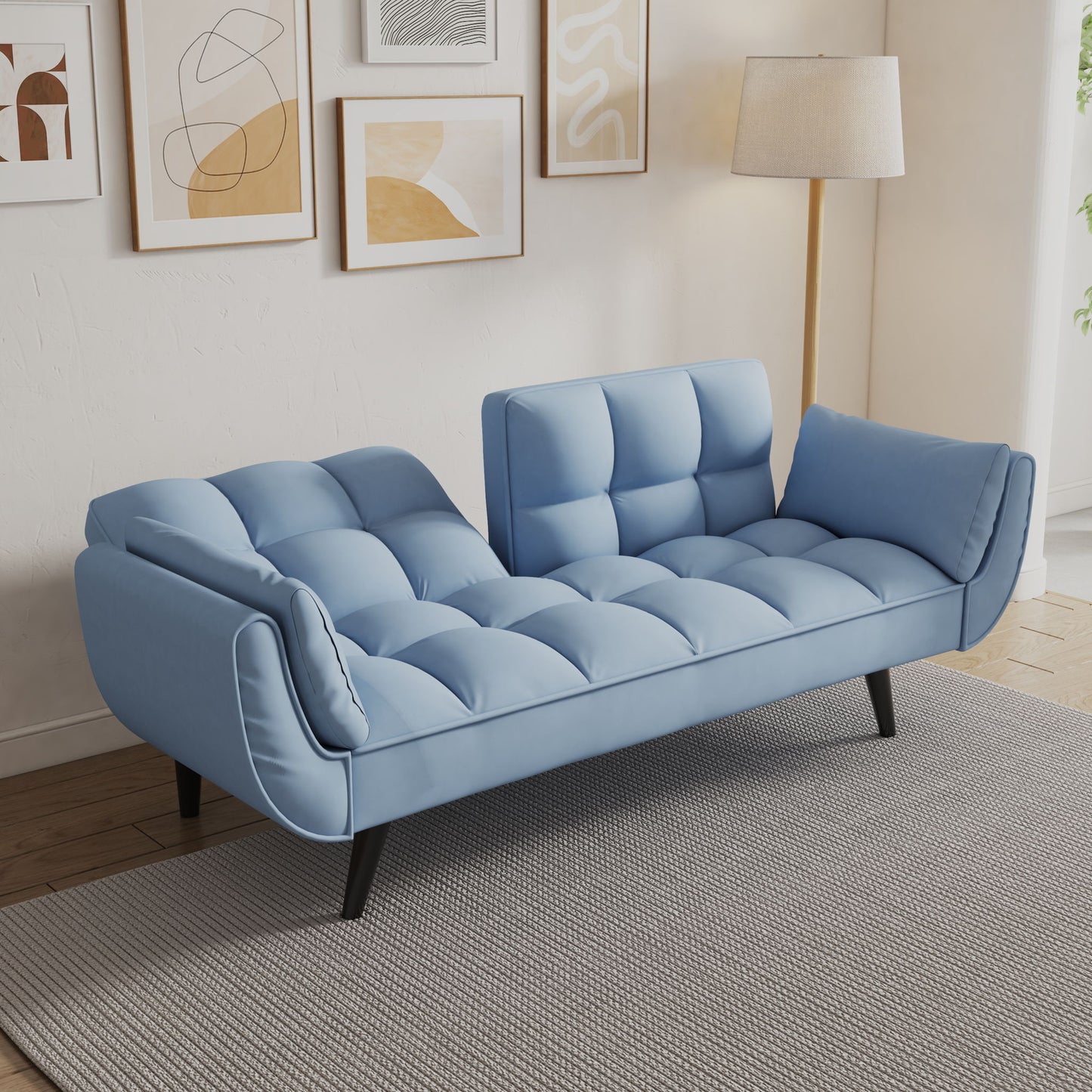The Sofa Soft has two armrests, throw pillows, and a comfortable fit, perfect for apartments or bedrooms. In a cozy living space, it sits on a gray rug with abstract wall art and a floor lamp behind it.