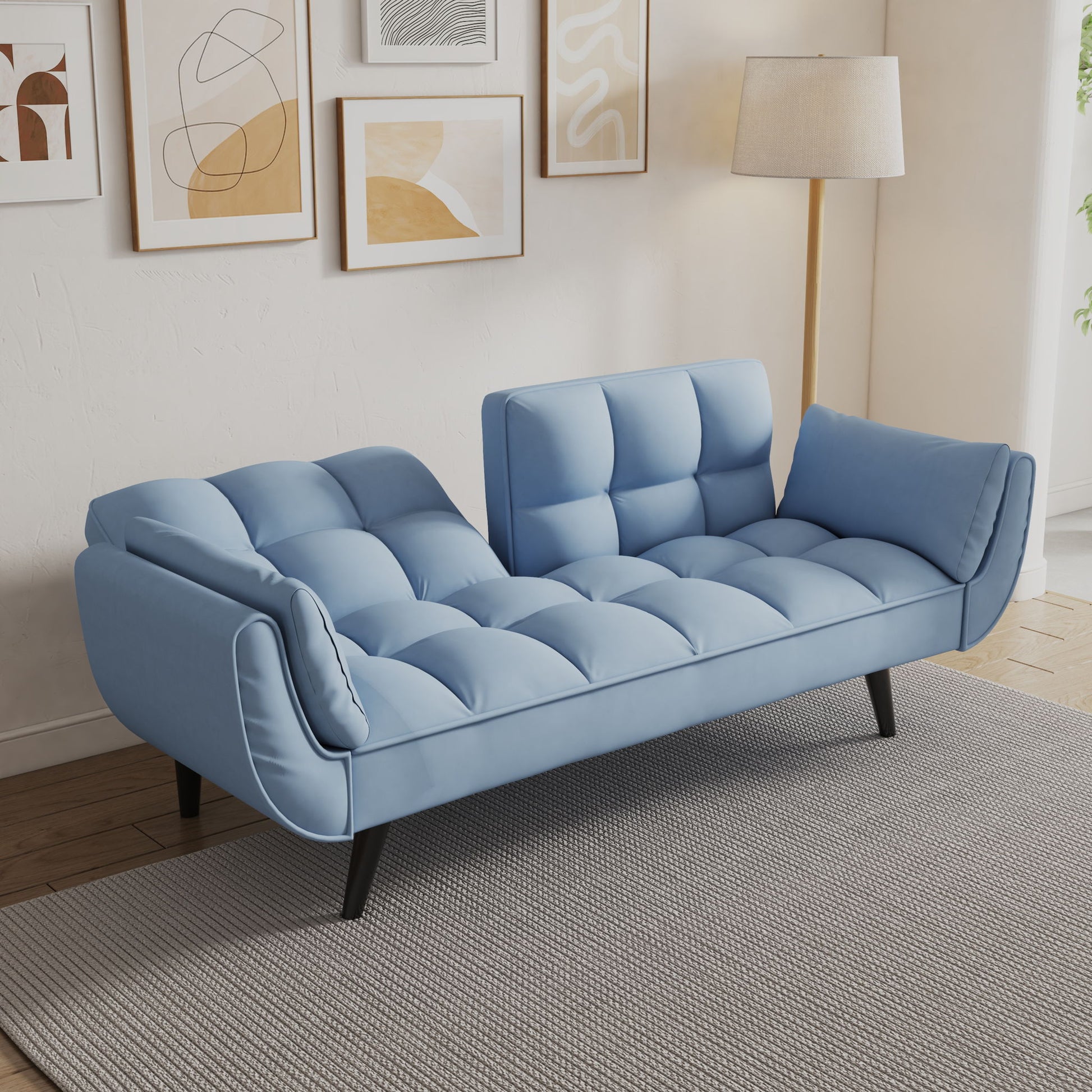 The Sofa Soft has two armrests, throw pillows, and a comfortable fit, perfect for apartments or bedrooms. In a cozy living space, it sits on a gray rug with abstract wall art and a floor lamp behind it.