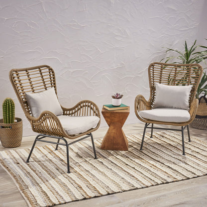 Two Modern Aesthetic Outdoor Rattan Accent Chairs with white cushions sit on a striped rug, facing a small wooden side table with a succulent. In the background, there’s a potted cactus and leafy plant against a textured white wall.