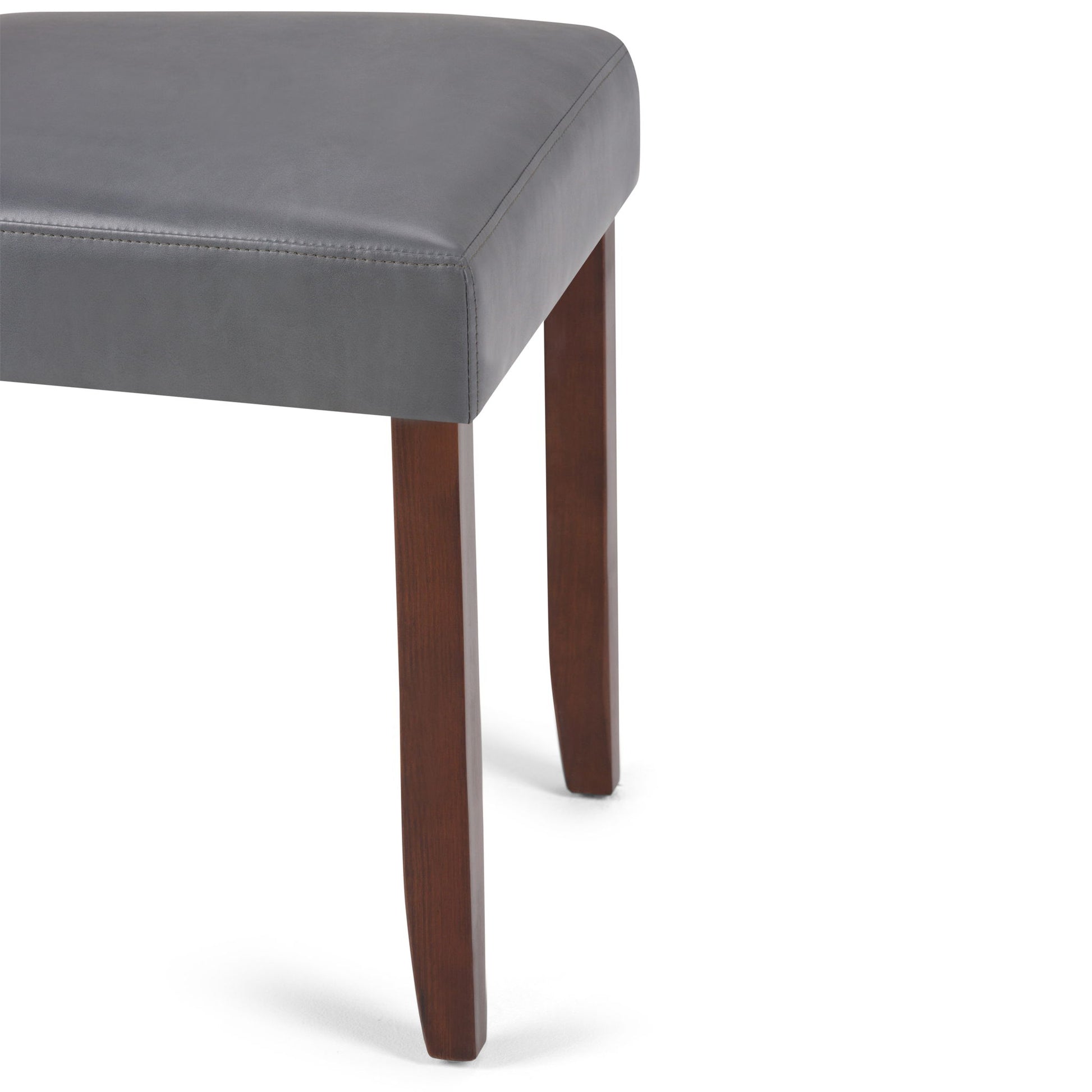 A close-up of the Acadian - Upholstered Parson Dining Chair (Set of 2) shows a gray cushion and two straight, dark wooden legs against a white background.