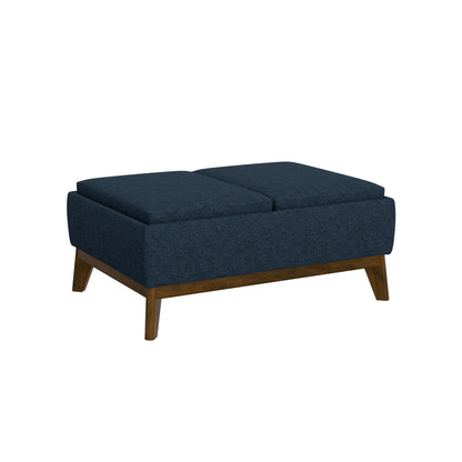 The Varia Reversible Tray Ottoman in blue features a rectangular upholstered design, wooden base with angled legs, and two cushioned sections on top.