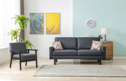A modern living room featuring the Bahamas - Sofa Set With 2 Throw Pillows, a dark gray armchair, colorful chevron pillows, a light rug, potted plant, wall art, clock, lamp, and wooden side table against blue and white walls.