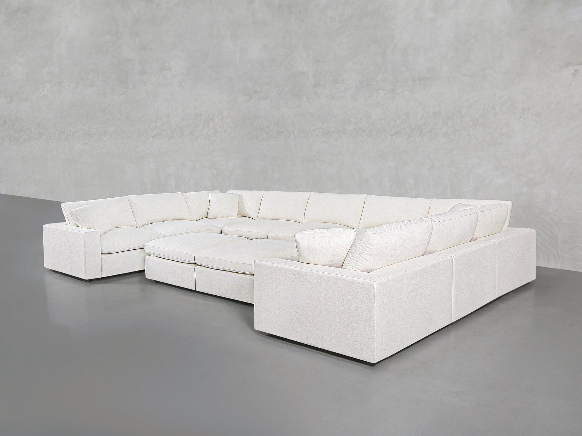 A spacious 9-Seat Modular U-Sectional with Double Ottoman in modern white, featuring plush cushions, sits against a plain light gray wall and floor in a minimalist room.