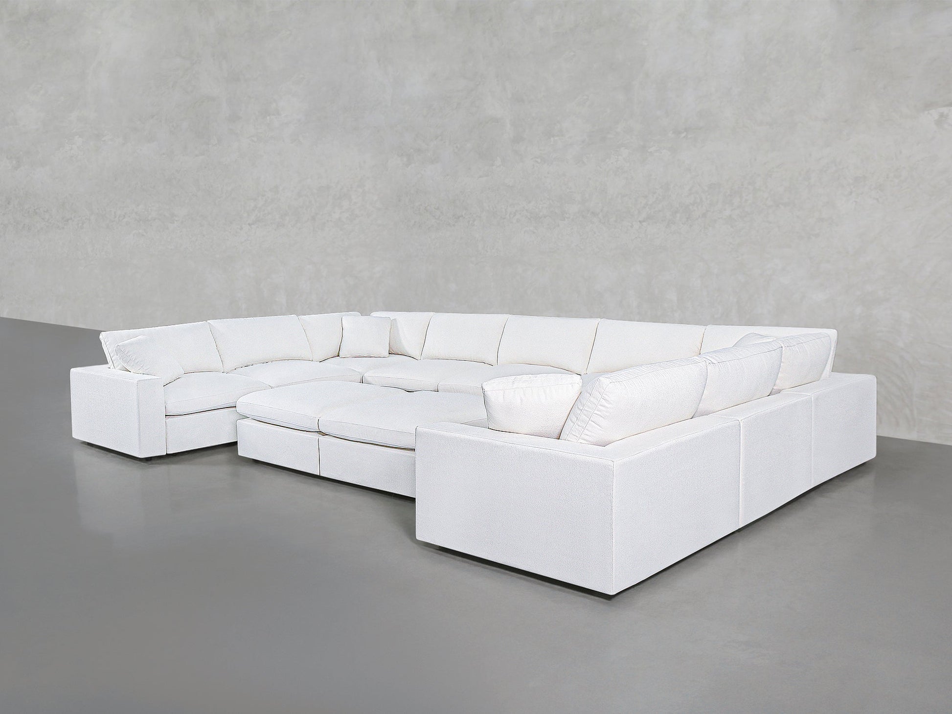 The 9-Seat Modular U-Sectional with Double Ottoman, in modern white with plush cushions, is arranged against a plain light gray wall and a smooth gray floor.