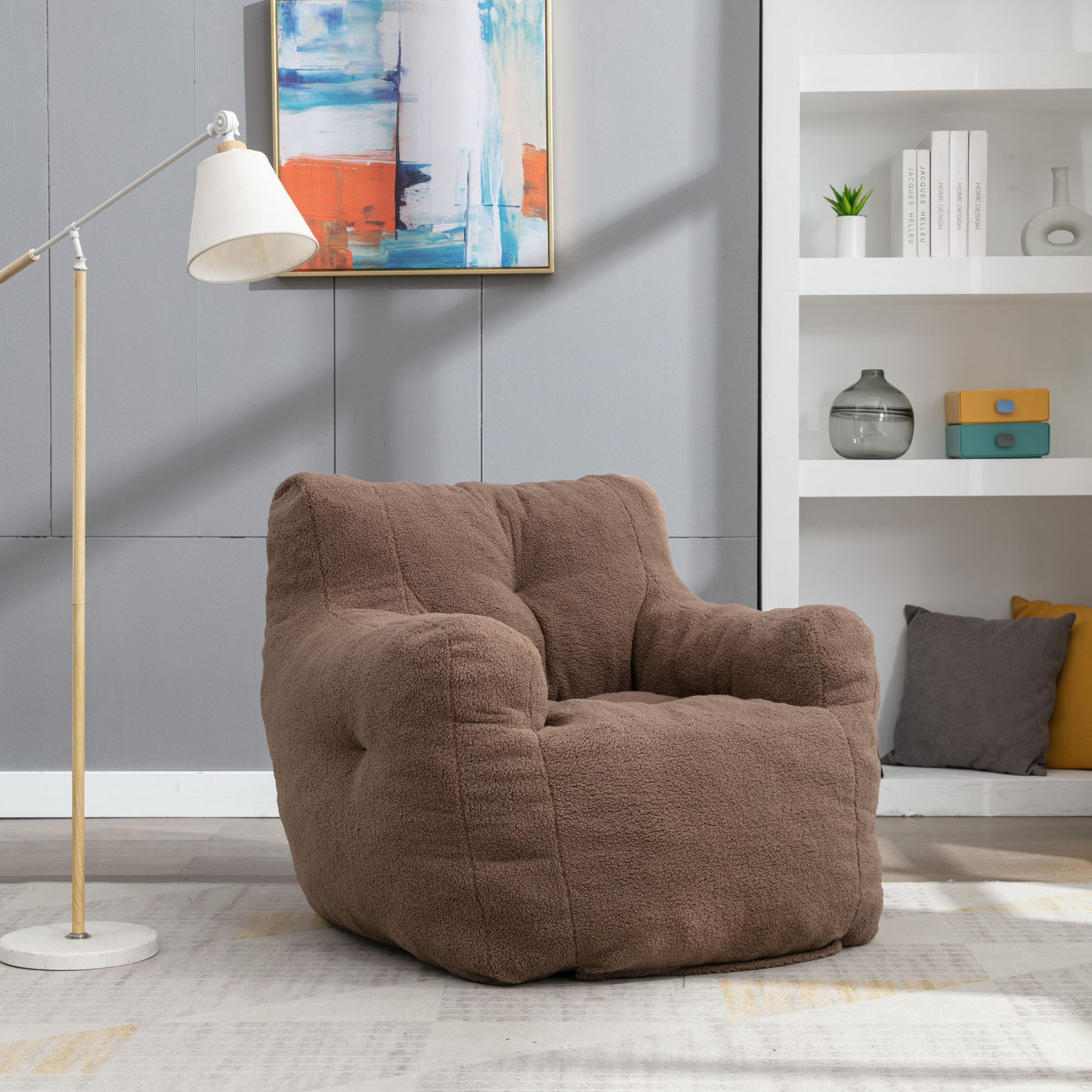 A Soft Teddy Fabric Tufted Foam Bean Bag Chair sits on a light rug in a modern living room, complemented by a floor lamp, abstract wall art, and shelves displaying books, plants, and decorative pieces in the background.