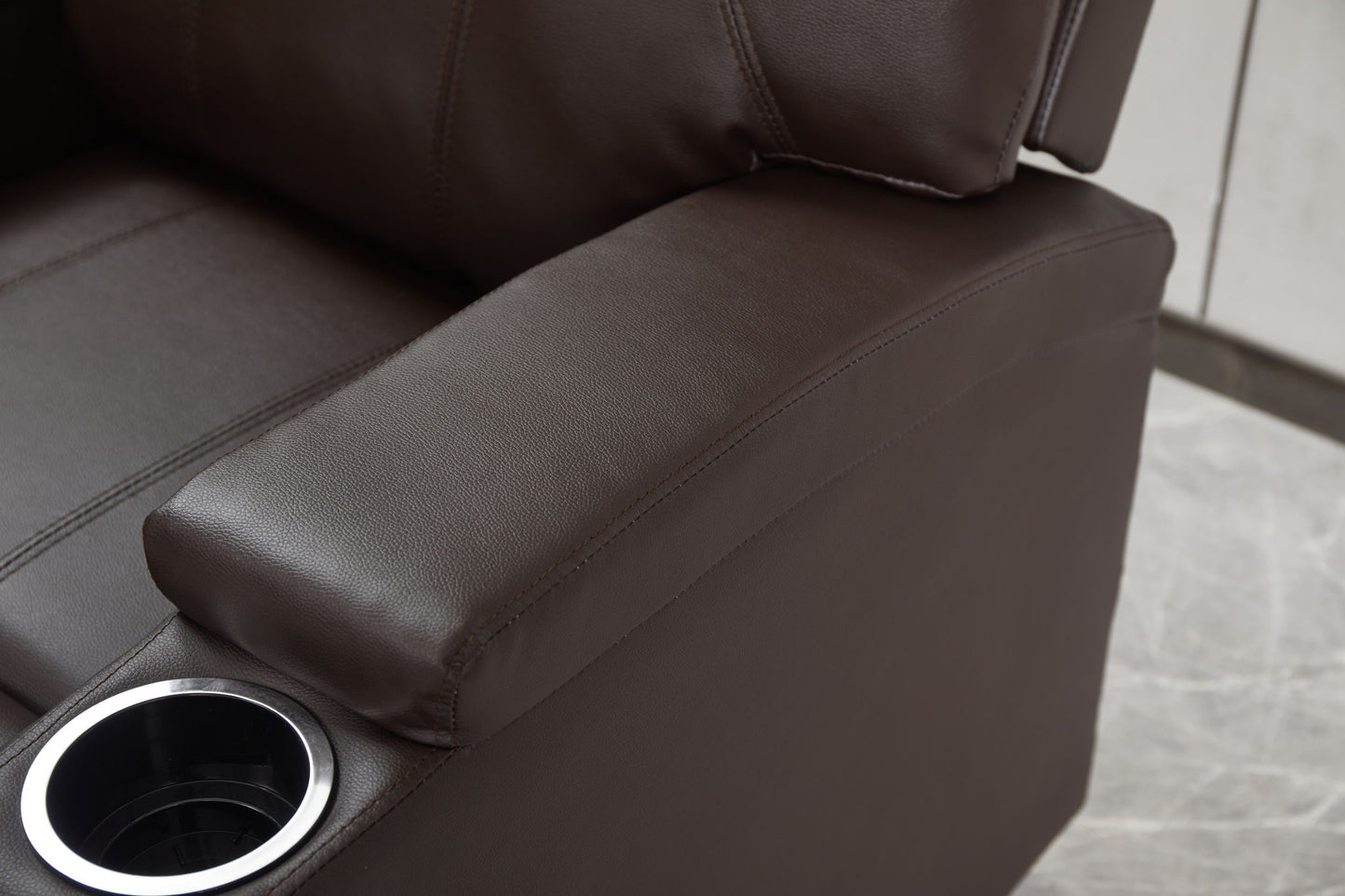 Close-up of the Modern Recliner Chair With Cup Holders, Remote Control, highlighting its brown leather armrest with built-in cup holder and part of the seat and backrest on a light-colored tiled floor.