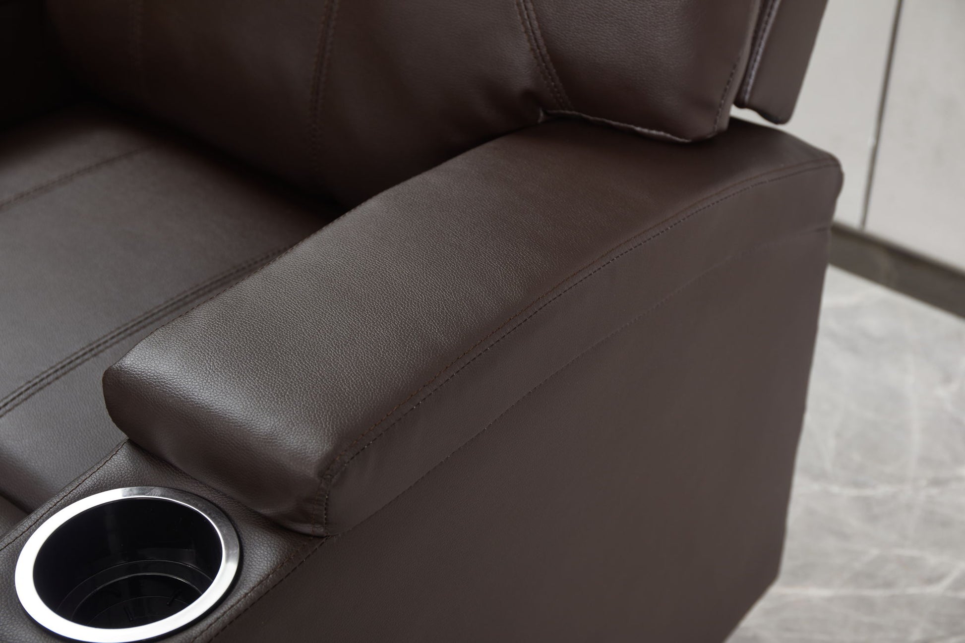 Close-up of the Modern Recliner Chair With Cup Holders, Remote Control, highlighting its brown leather armrest with built-in cup holder and part of the seat and backrest on a light-colored tiled floor.