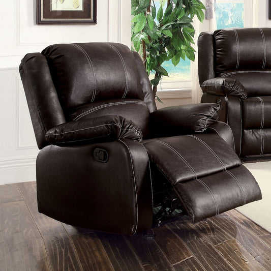 The Zuriel Synthetic Leather Recliner Chair, in dark brown with padded arms and backrest, sits on a wooden floor in a bright living room beside a matching sofa and a green leafy plant.