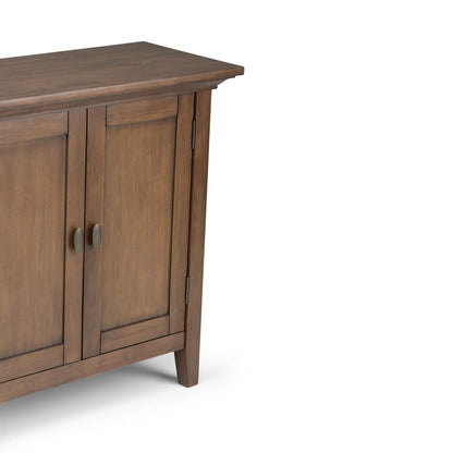 A partial view of the Redmond - Handcrafted Low Storage Cabinet featuring two paneled doors, metal knobs, and tapered legs, set against a white background.