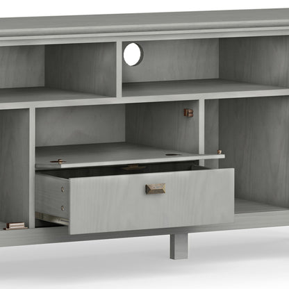 The Artisan TV Media Stand is a gray wooden unit featuring multiple open shelves, a round cable management hole on the back panel, and a centrally located drawer that's partially open.