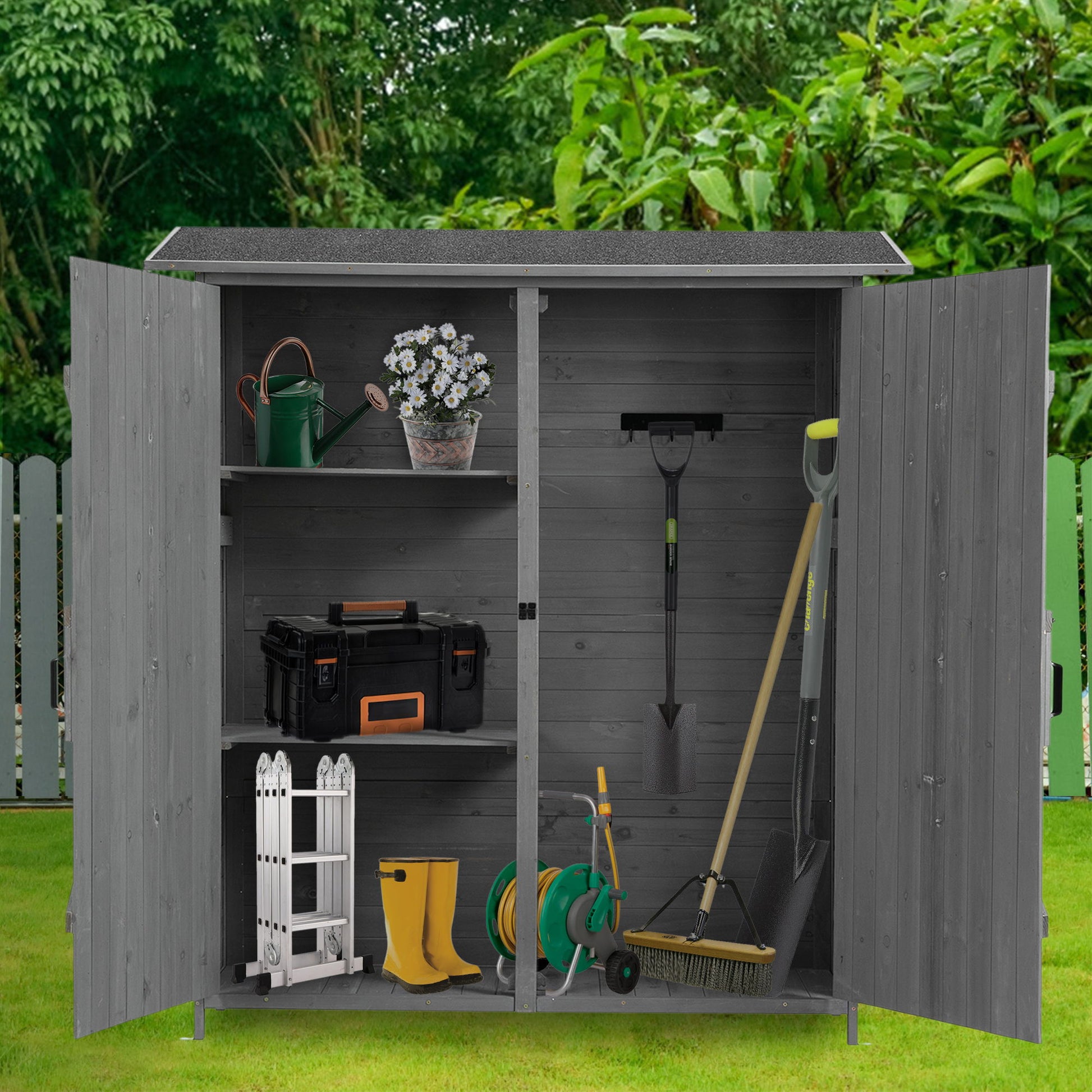The Outdoor Storage Shed with Lockable Door and Detachable Shelves features open doors showing gardening tools, a toolbox, yellow boots, a watering can, potted plant, hose, small ladder, and hanging tools; set on grass with trees and a white fence behind.