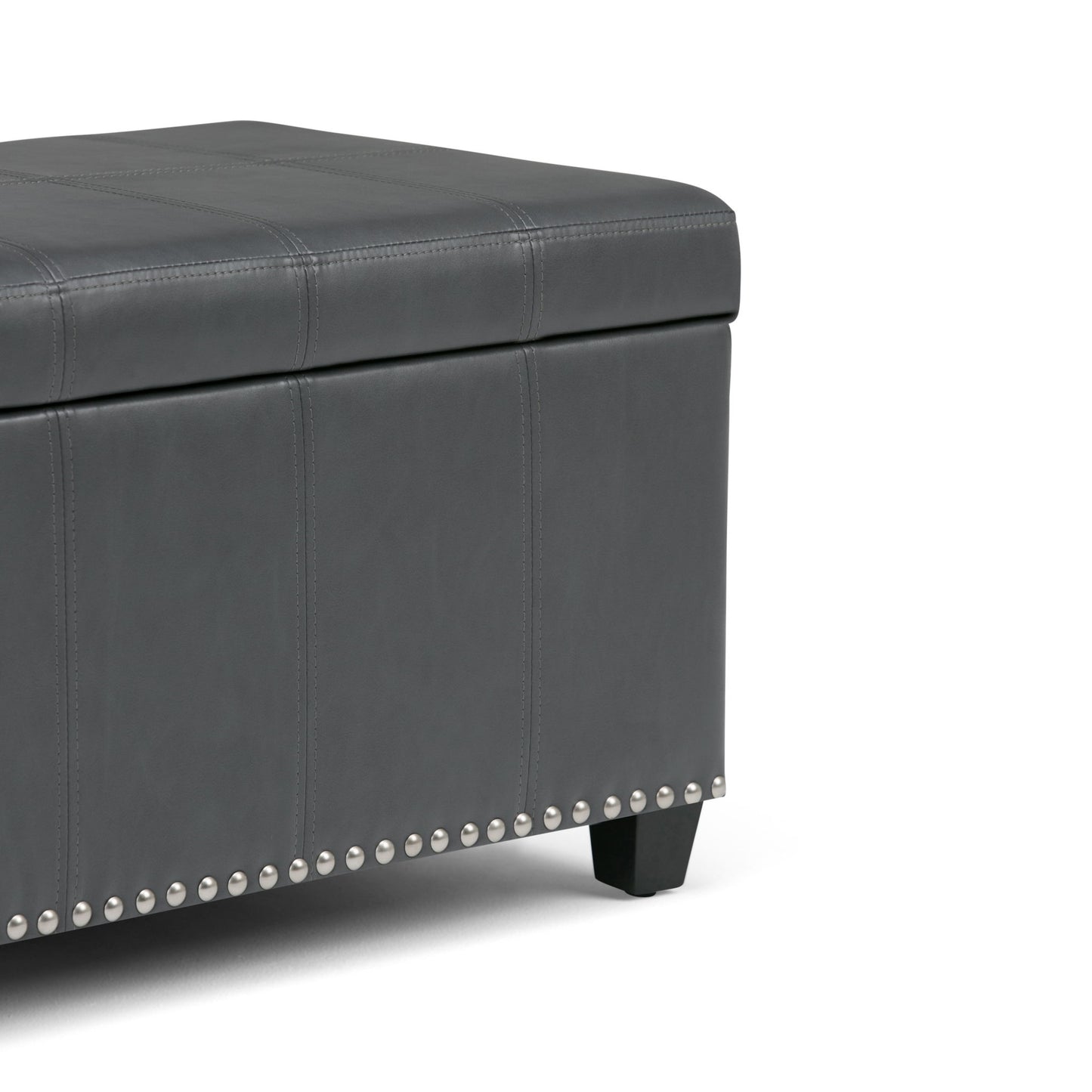 A close-up of the Amelia - Transitional Storage Ottoman Bench features gray upholstery, visible stitching, silver nailhead trim at the base, and short black legs.