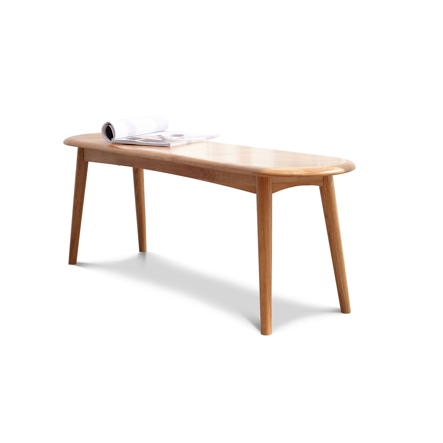The Dining Bench, Table Bench For Living Room features four angled legs, rounded corners, and a smooth finish. An open magazine sits on top of the bench against a plain white background.
