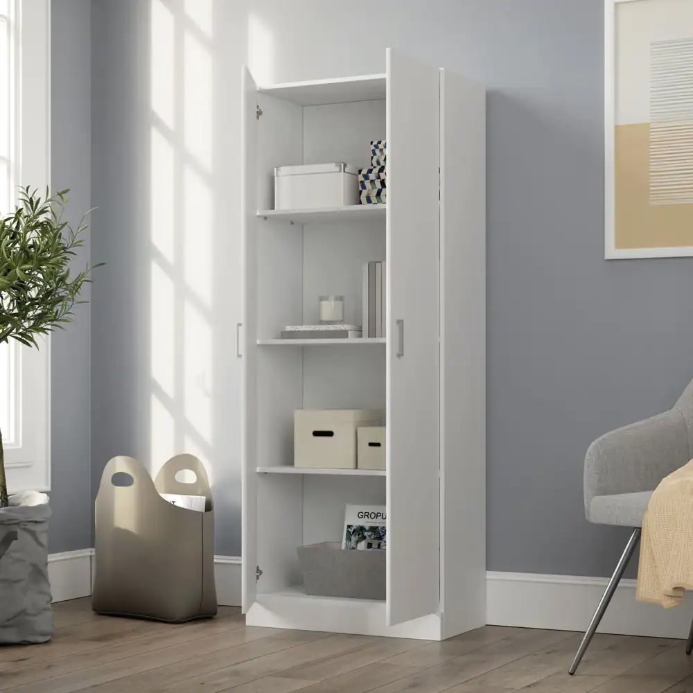 The Alara - Height Simplistic Modern Double Door Storage Cabinet in white stands against a gray wall in a bright room, its open doors revealing shelves with boxes, books, and decor. A beige storage bin sits on the floor near a large window and plant.