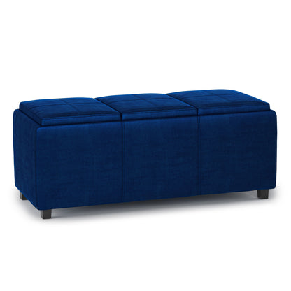 The Avalon Upholstered Storage Ottoman features a rectangular design in deep blue fabric, three cushioned sections, and short black legs, shown against a white background.