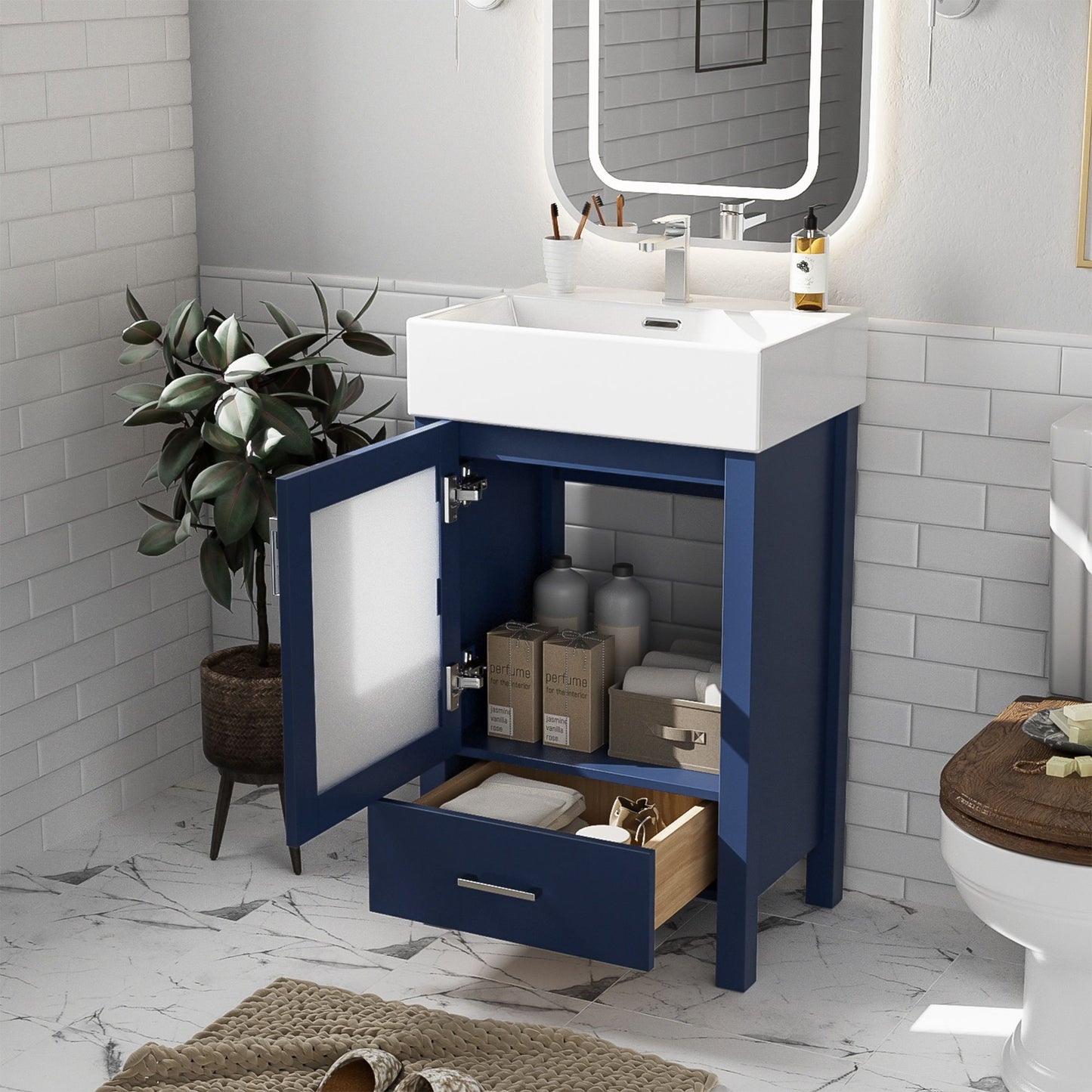 A modern bathroom features the Bathroom Vanity With Ceramic Sink And Ample Storage, Ideal For Small Bathrooms. The blue vanity has open doors showing storage boxes with soap and towels. A plant is in the corner, with a mirror above and a toilet to the right on marble tile floors.
