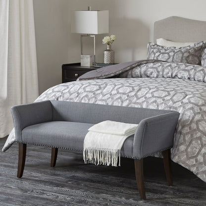 A modern bedroom featuring a gray patterned bed, wooden floors, a dark nightstand with a lamp and white flowers, plus the Elegant Design Bench Upholstery with a solid wood frame and white throw at the foot of the bed.