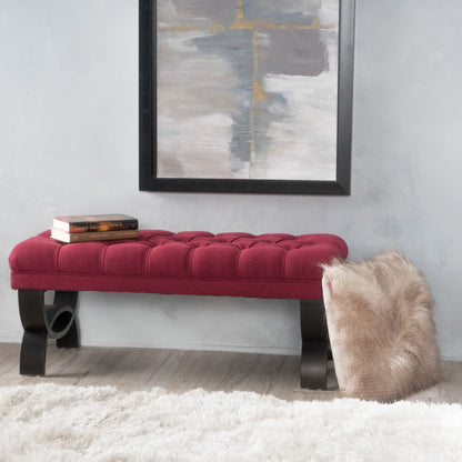 The Hilton - Ottoman Bench Classic Style, featuring a red tufted seat and black curved legs, sits in front of a gray wall under an abstract painting. A fur throw is draped over one end, two books rest on the other, and a white rug covers the floor.