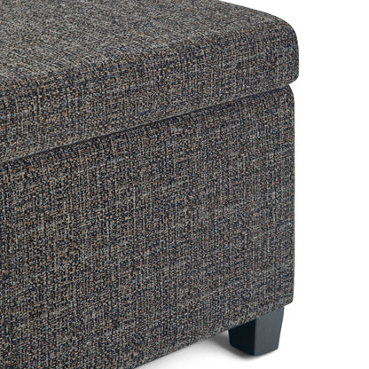 Close-up of the corner of the Avalon Storage Ottoman Bench in dark gray, featuring textured fabric upholstery and short black wooden legs, shown against a white background.