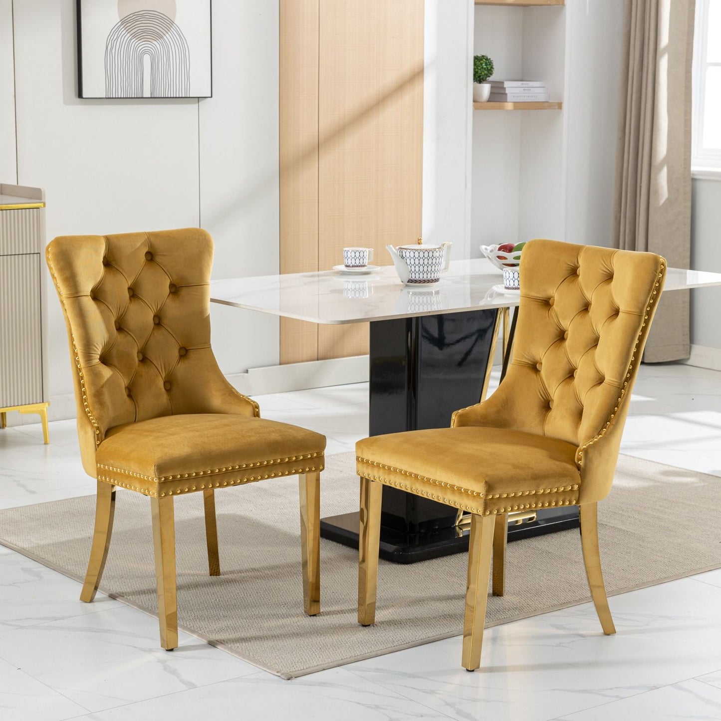 A set of two Nikki modern velvet upholstered dining chairs with golden stainless steel legs and nailhead trim in a room.