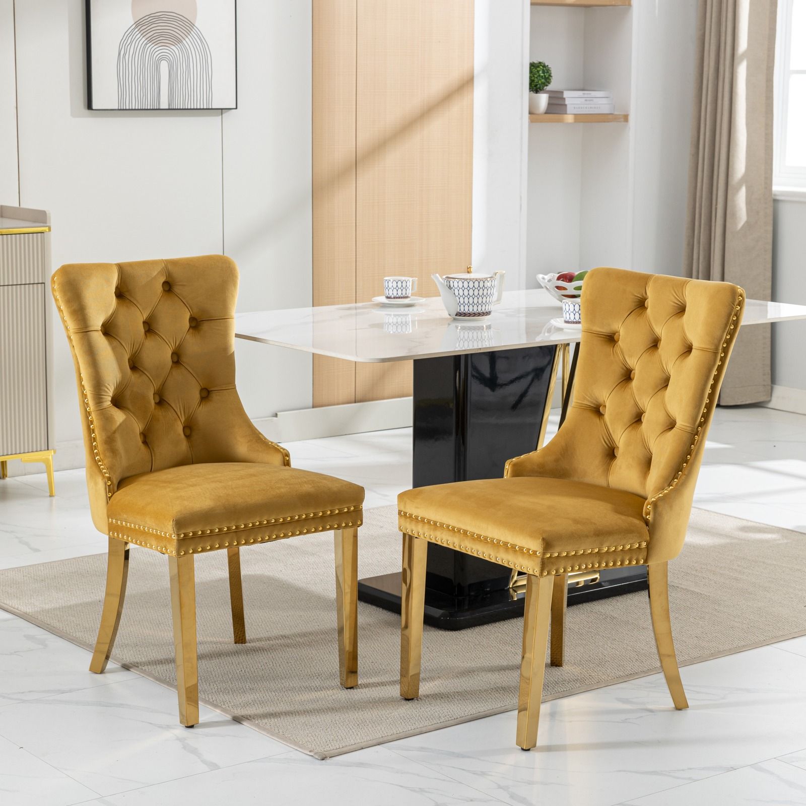 A set of two Nikki modern velvet upholstered dining chairs with golden stainless steel legs and nailhead trim in a room.