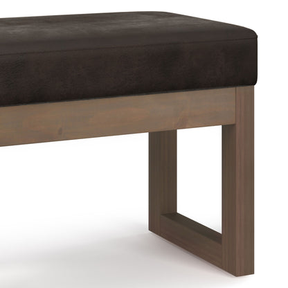 Close-up of the Milltown - Upholstered Ottoman Bench featuring a dark brown cushioned seat and wooden legs in a rectangular, open-frame design. Set against a plain white background.