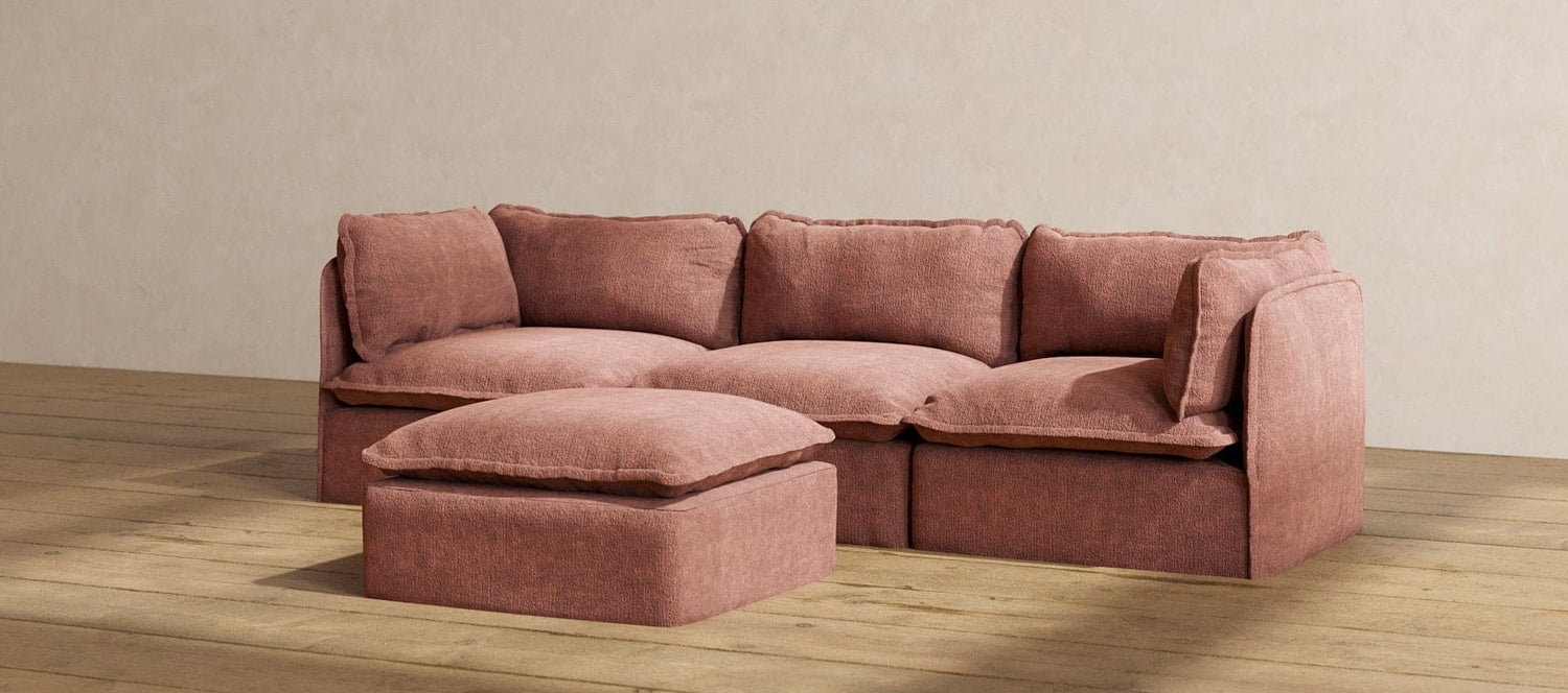 A cozy, light brown sectional sofa with a matching ottoman placed on a hardwood floor. The sofa features plush cushions and a minimalist design, blending comfort with modern aesthetics against a plain beige wall.