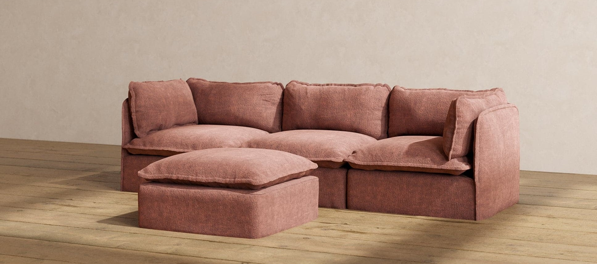 A cozy, light brown sectional sofa with a matching ottoman placed on a hardwood floor. The sofa features plush cushions and a minimalist design, blending comfort with modern aesthetics against a plain beige wall.