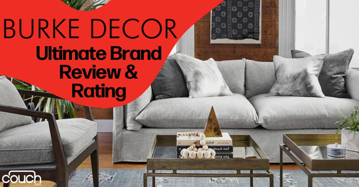 A modern living room with a gray sofa surrounded by stylish wooden and metal furniture. Decorative pillows and throws are on the sofa. Text on a red overlay reads "Burke Decor Ultimate Brand Review & Rating" with a "Couch" logo at the bottom left.