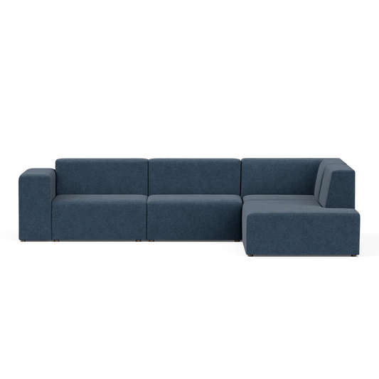 The Four-Seater Form Sectional is an L-shaped sofa in navy blue, featuring a minimalist design with flat backrests and armrests. Its spacious seating sits elegantly against a neutral background, making it perfect for modern living rooms.