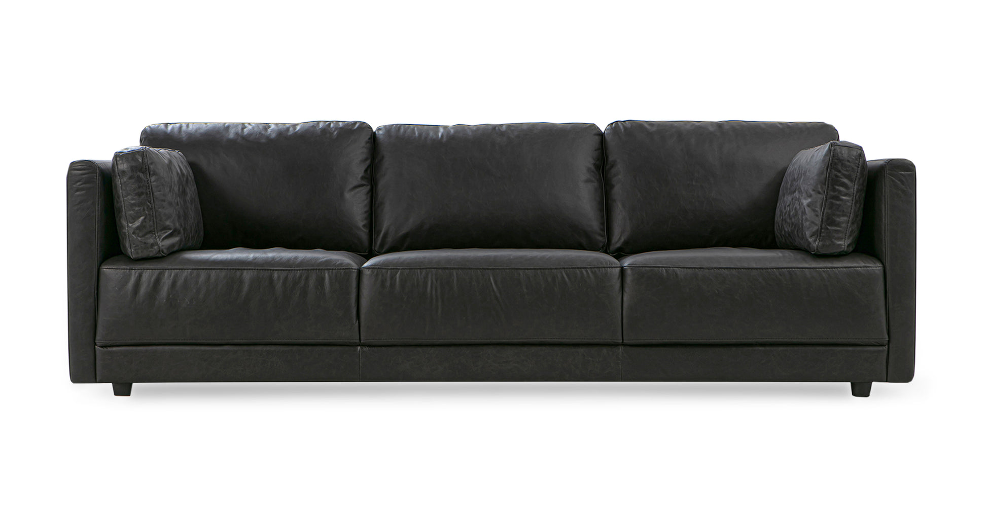 The Domus 93" Leather Sofa in chestnut is displayed, featuring a modern design with straight lines, three seat cushions, and two matching throw pillows. It incorporates a sleek and minimalistic style with a low backrest.