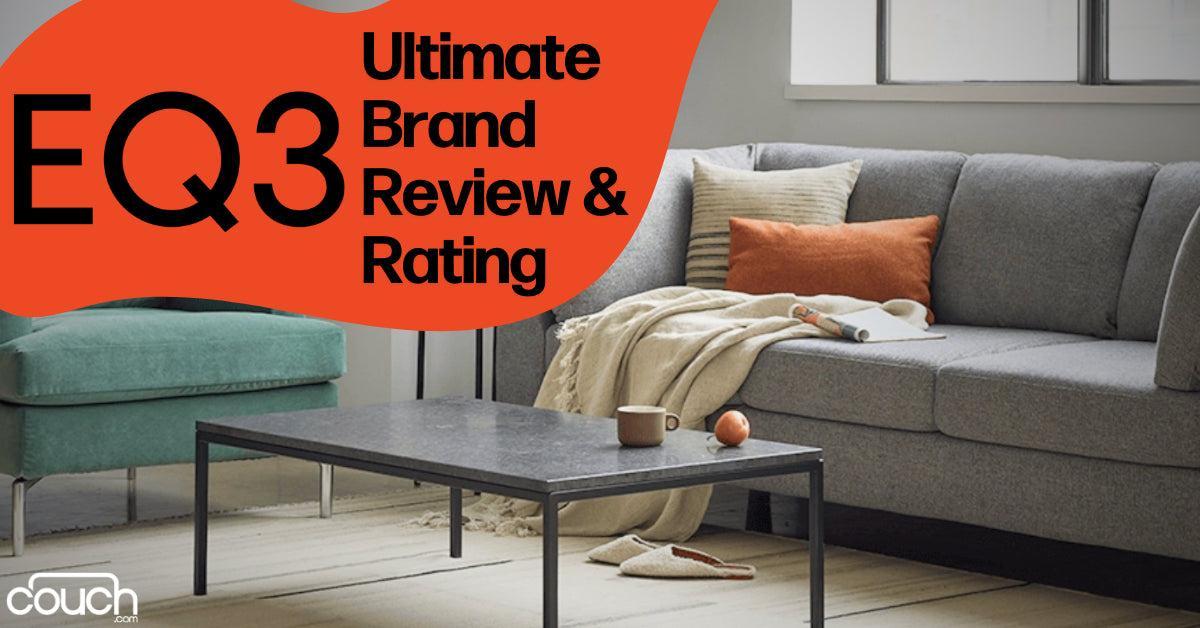 A modern living room features a gray sofa with pillows and a beige blanket. A black coffee table in front of the sofa holds a cup and book. The wall has large windows. Text overlay reads "EQ3 Ultimate Brand Review & Rating" with a logo in the corner.