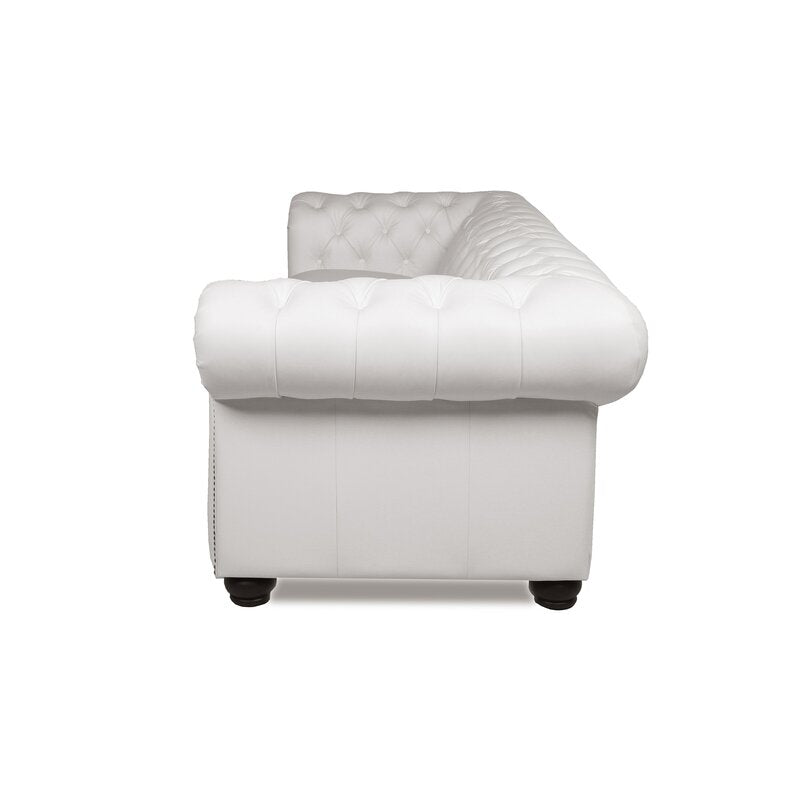 Side view of a white Birch Lane Freddie 95'' Leather Sofa on black legs. The back and armrests feature deep button detailing, giving it a classic, luxurious look. The sofa is set against a plain white background.