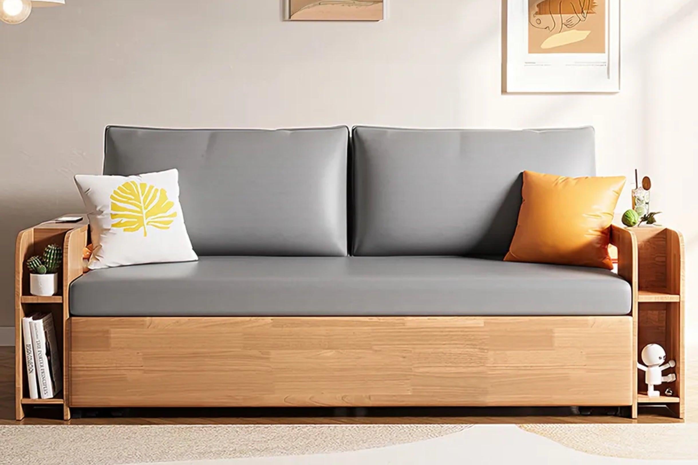 Modern sofa with light gray cushions and wooden frame, featuring side storage shelves. A white pillow with a yellow leaf design and an orange pillow are on the sofa. Neutral wall background with framed art. Small plants are positioned on the side shelves.